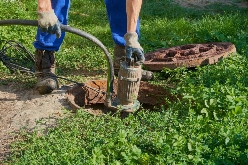a man holds a vacuum pump over a cesspool, pumping out a home septic tank with a pump