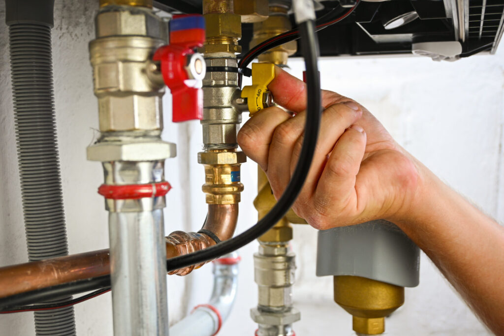 Hand turning a yellow valve on complex plumbing pipes in a boiler system.