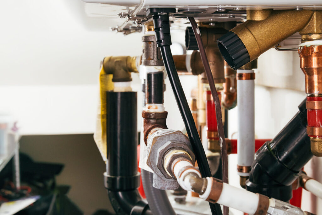 Plumbing underneath hot water heating system. Piping for a natural gas–powered heater in a closed-loop hydronic system. Plumbing service for home heating and maintaining. Selective focus.